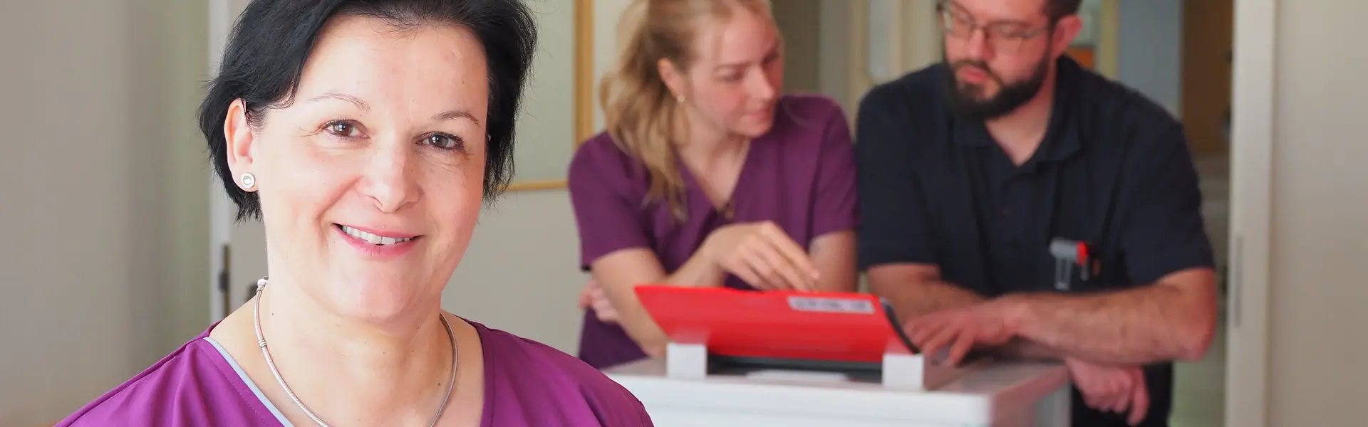 Lächelnde Pflegerin im Vordergrund, ein Pfleger und eine Pflegerin im Hintergrund